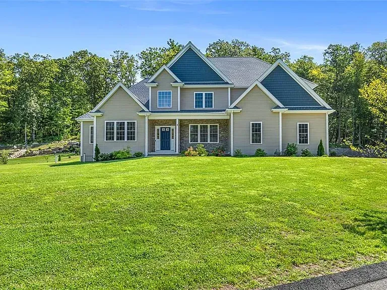 Beige two-story house with blue roof and door, set on a green lawn surrounded by trees.