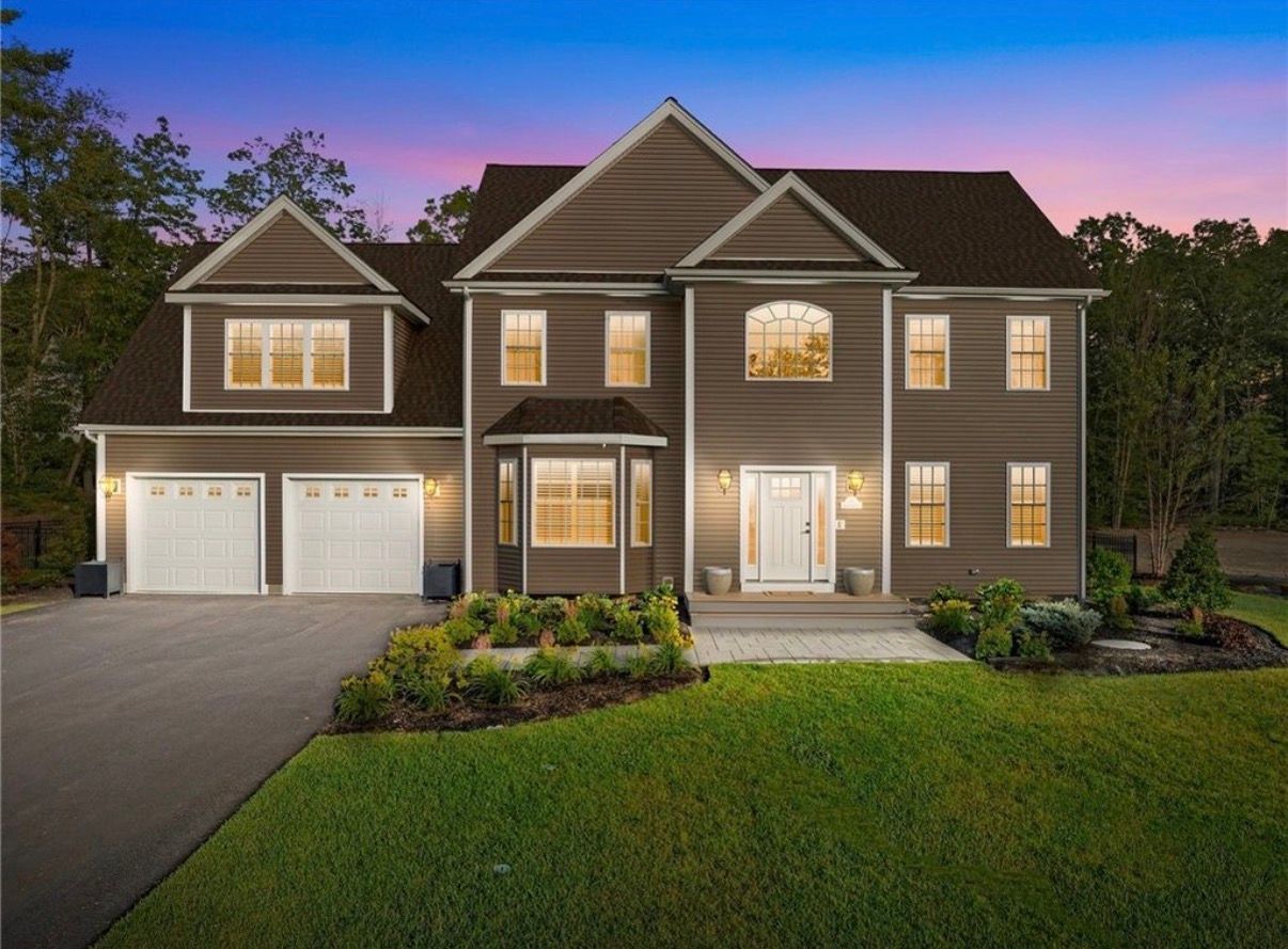 Two-story house with light-colored siding, front porch, and grassy yard under a blue sky.