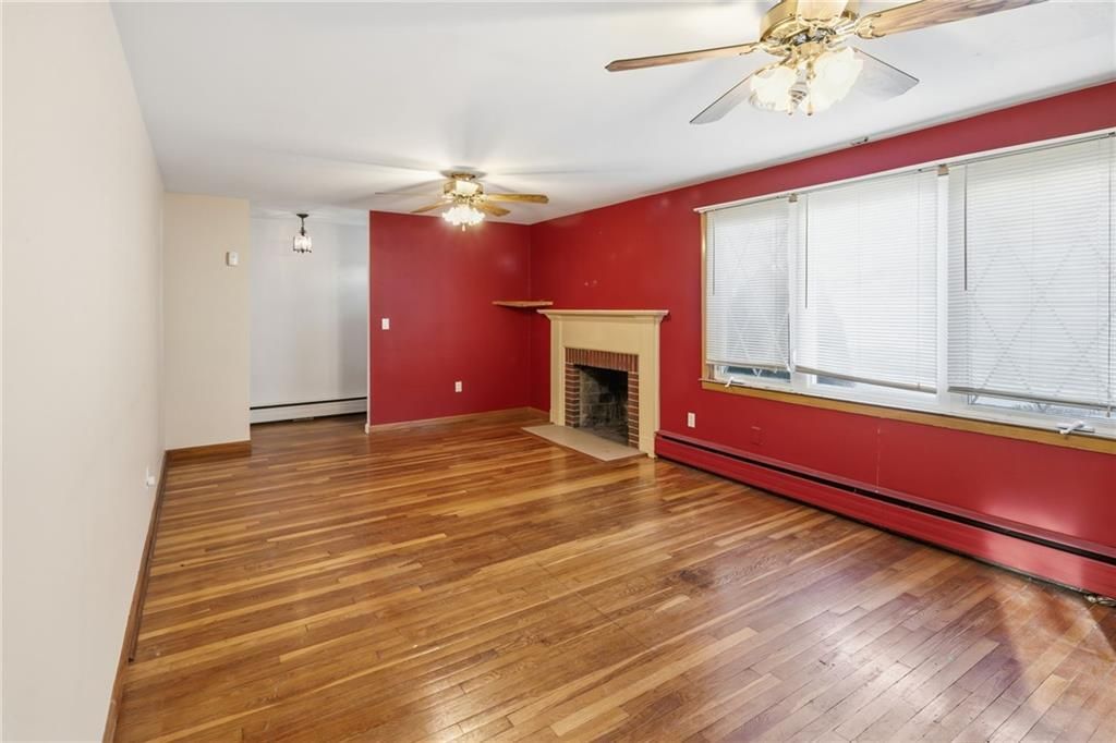 Empty living room with wood floors, red wall with fireplace, and two ceiling fans.