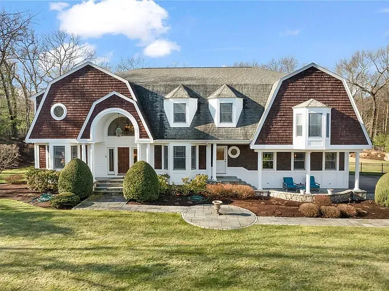 Dutch colonial-style house with brown roof and dormers, white siding, and manicured lawn.
