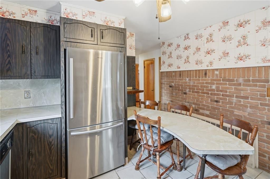 Kitchen with stainless steel refrigerator, dark cabinets, a long dining table, and exposed brick wall.