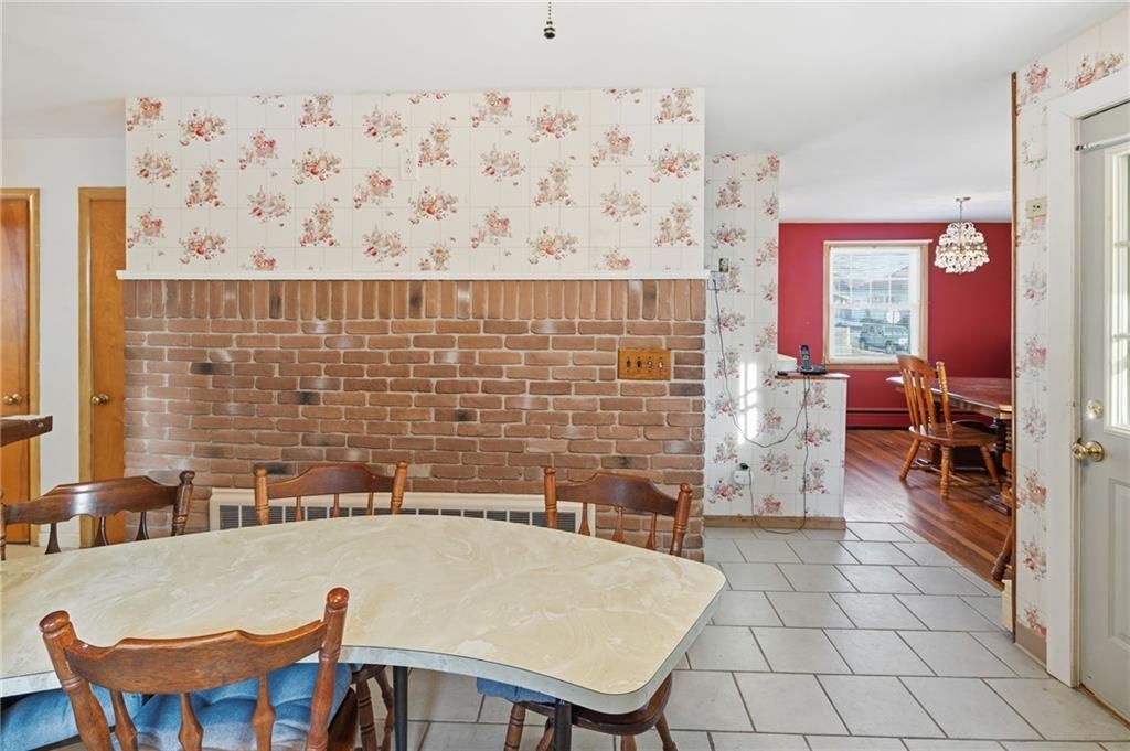 A dining room with a large table, chairs, and brick wall. Floral wallpaper, tiled floor, and a red dining area are visible.