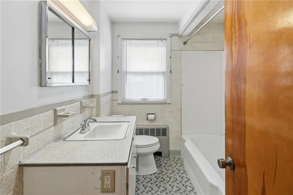 Bathroom with a white vanity, toilet, and bathtub. The floor has a black and white pattern.