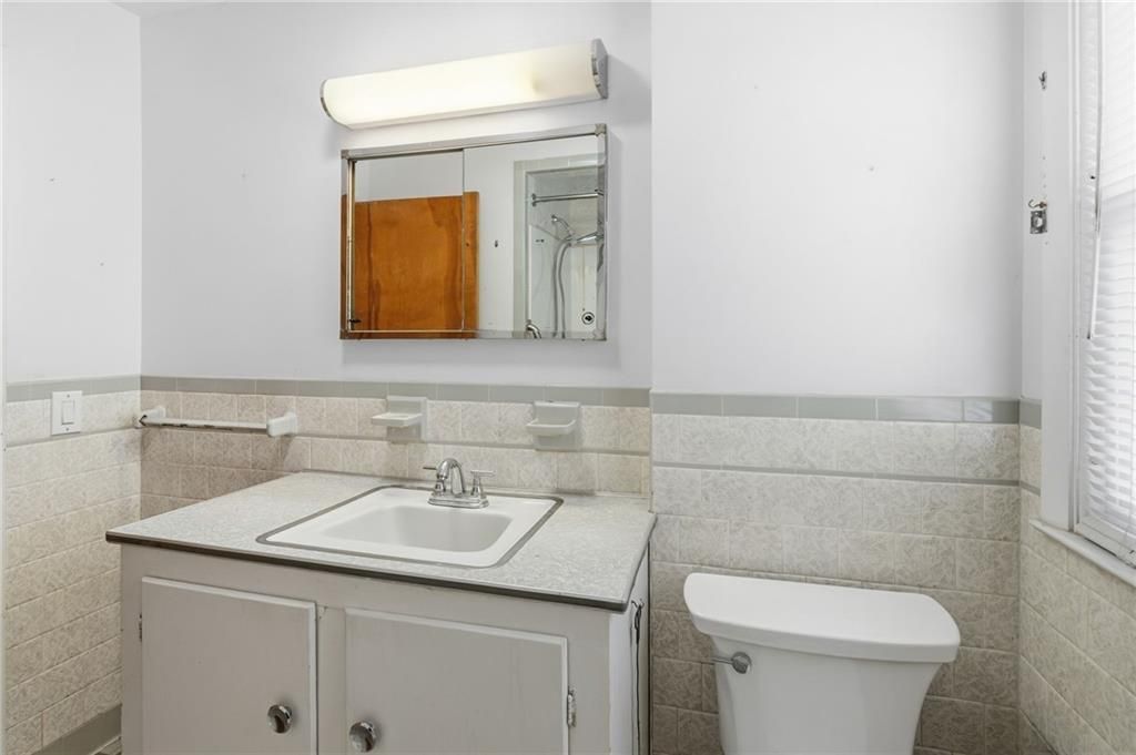 Bathroom with a white toilet, vanity, and mirror with light fixture.
