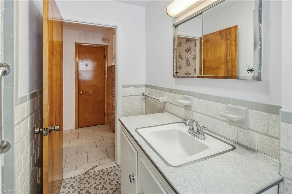 Bathroom with white sink, gray countertop, and white and gray tiled walls. Wooden door and medicine cabinet.