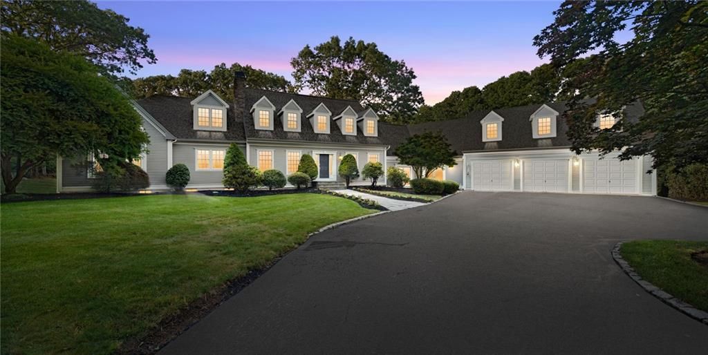 Exterior view of a large, light-colored house with a long driveway at dusk.
