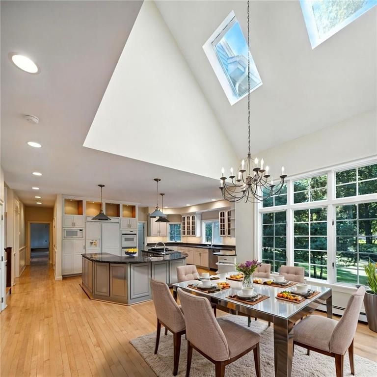 Spacious kitchen/dining area with skylights, large windows, chandelier, wooden floors and light-colored cabinets.