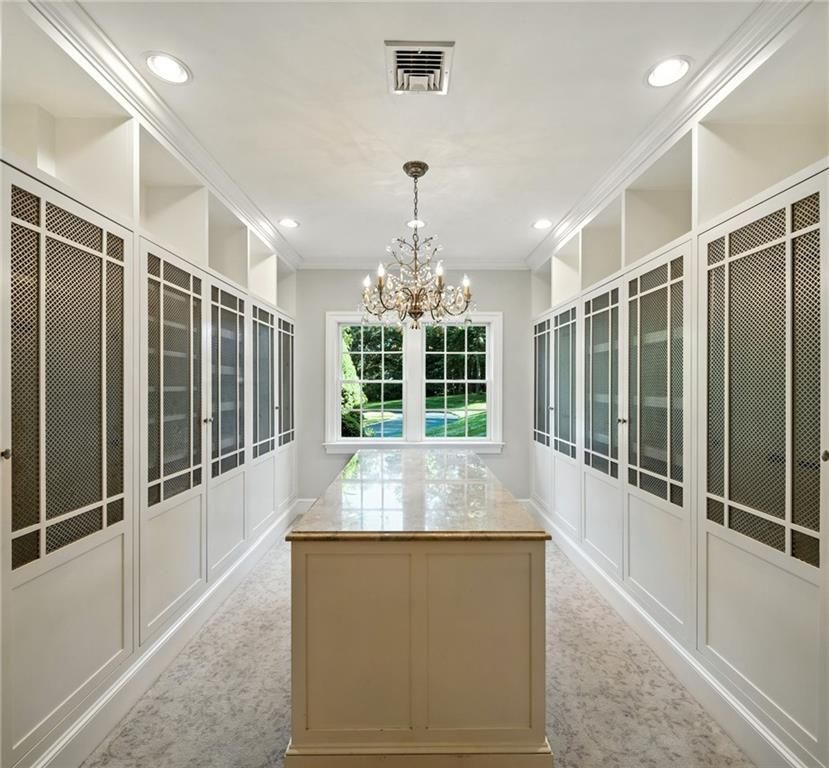 Luxurious white walk-in closet with island, chandelier, window, and built-in storage.