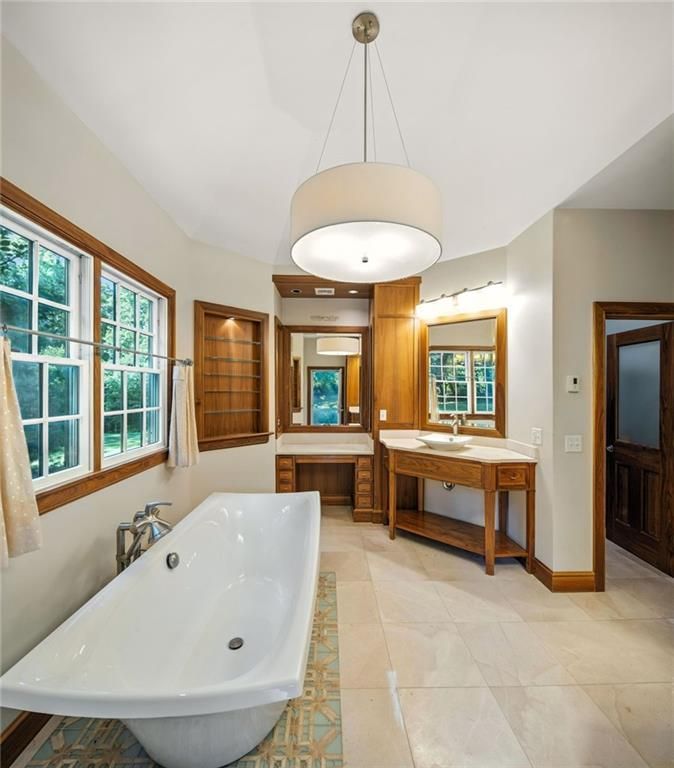 Spacious bathroom with a white tub, wooden accents, and a large circular light fixture.