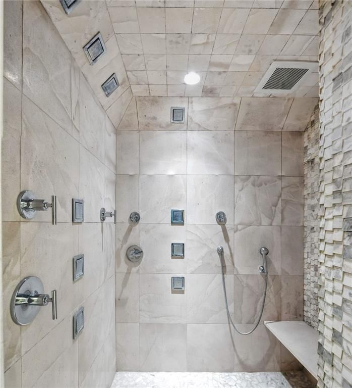 Luxurious tiled shower with multiple showerheads and controls; white and gray color scheme.