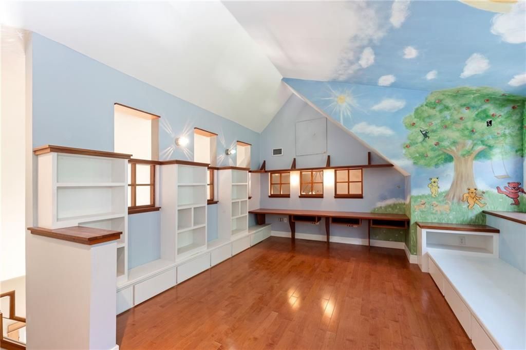 Playroom with built-in shelves and desk. Mural of a sunny sky and tree. Hardwood floor.
