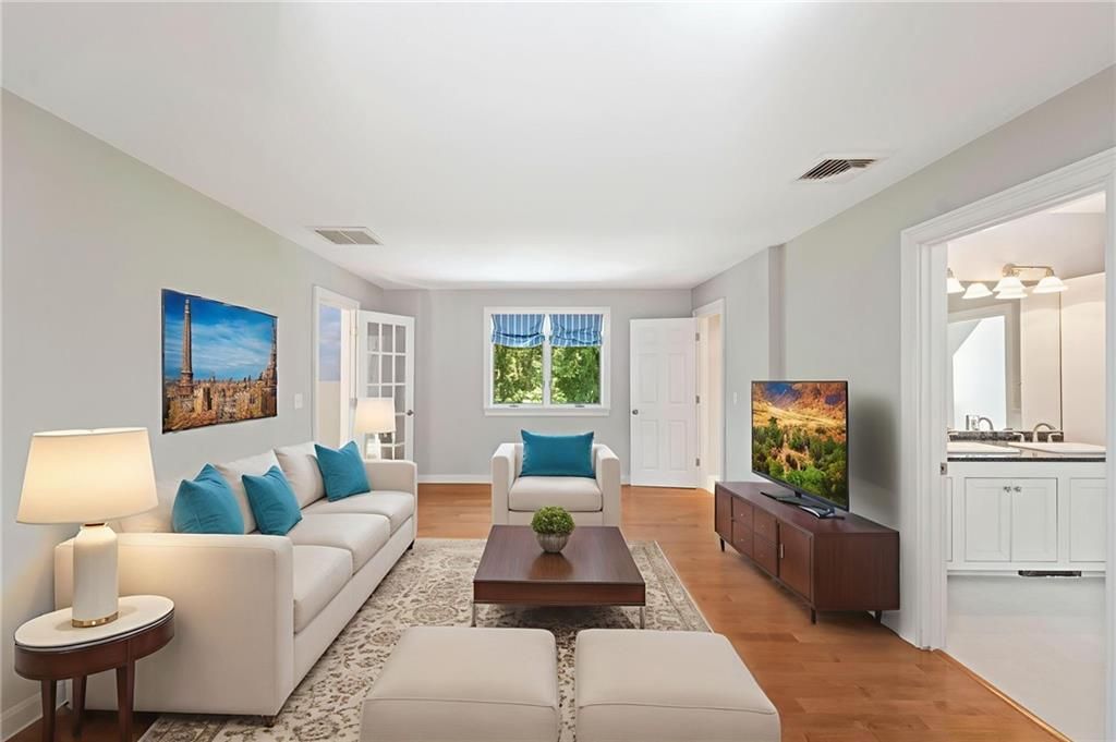 Bright living room with white sofas, blue pillows, wood floors, and a TV.