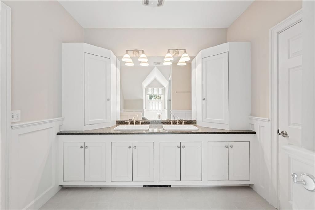 White bathroom with double vanity, cabinets, and mirror.