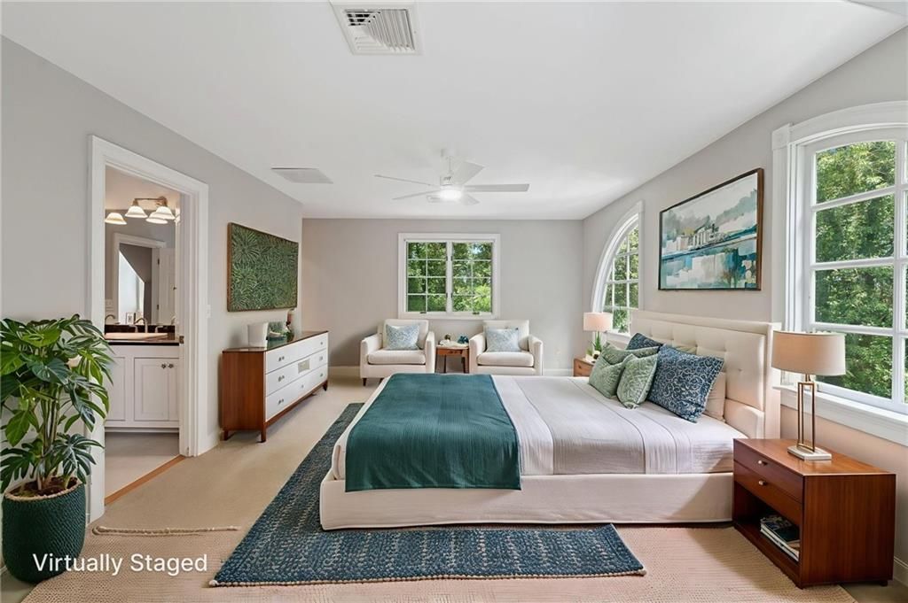 Spacious bedroom with white walls, bed, sitting area, and large windows looking out to trees.
