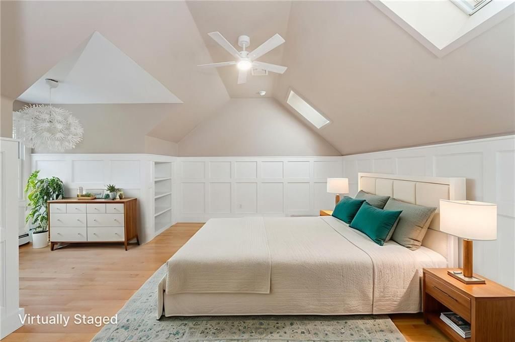 Bedroom with vaulted ceiling, king bed, neutral colors, white paneling, wooden bedside tables, ceiling fan.