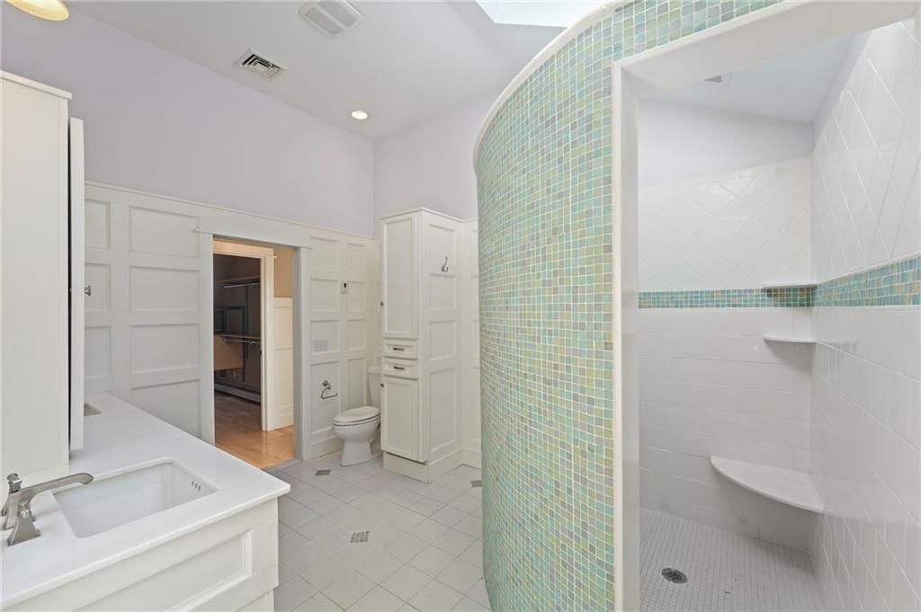 Spacious white bathroom with curved teal tile shower. White vanity, toilet, and cabinets.