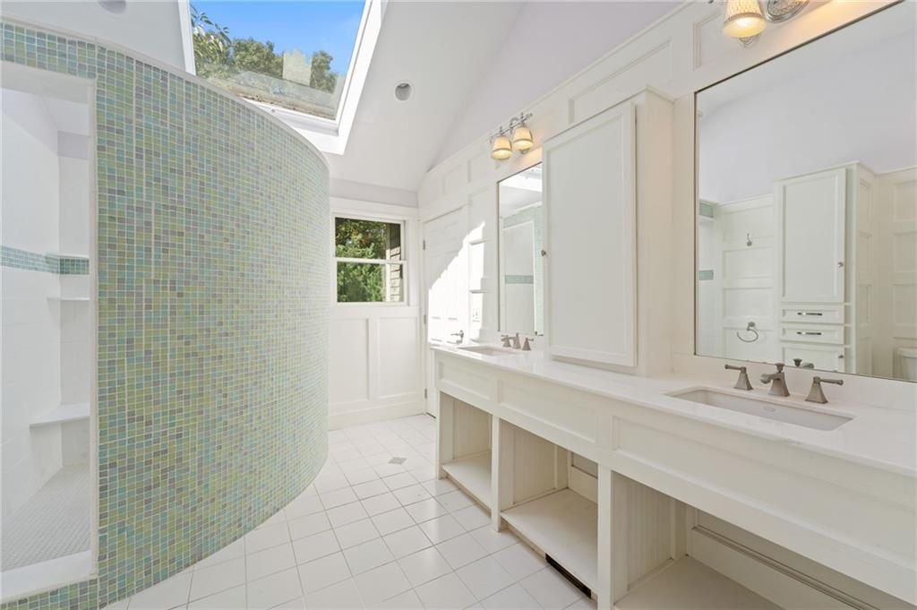 Spacious white bathroom with a curved, mosaic-tiled shower, skylight, and double vanity.