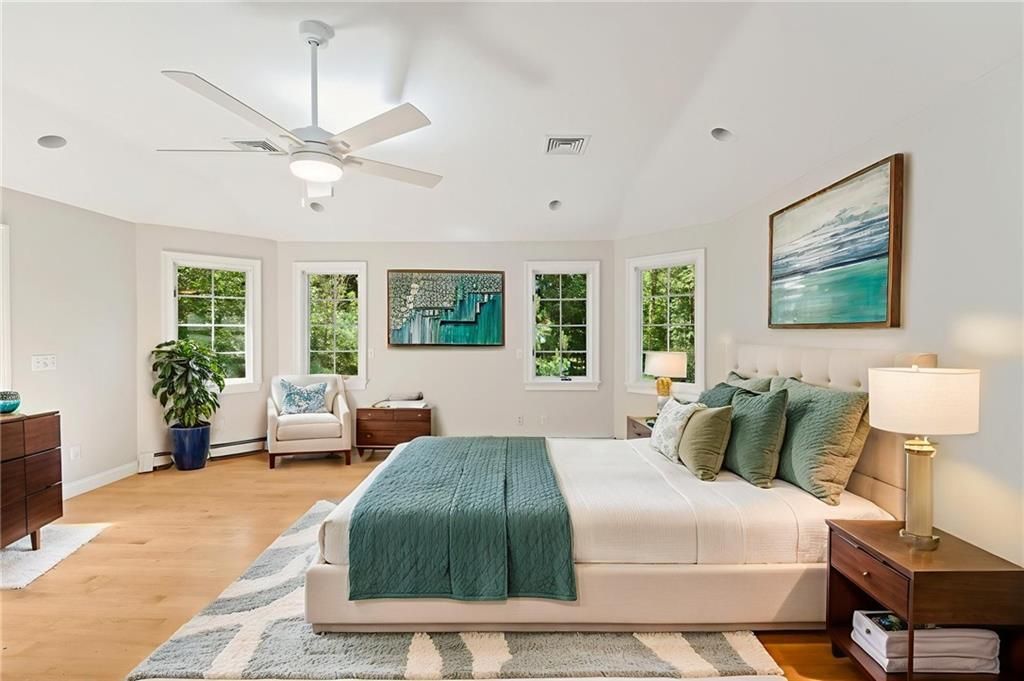 Spacious bedroom with a bed, windows, artwork, and a ceiling fan. Teal and light colors dominate.