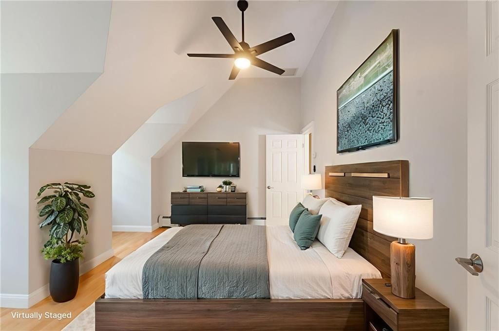 Bedroom with wood bed, nightstand, and dresser. Gray walls, ceiling fan, and large plant.