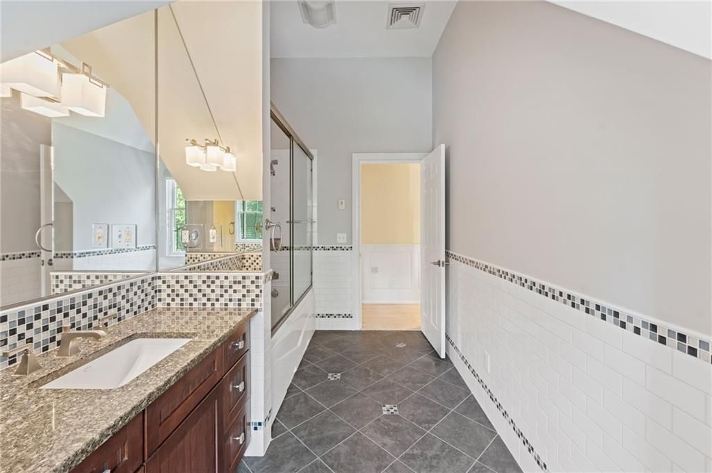 Bathroom with large mirror, dark granite vanity, mosaic tile, and a door.