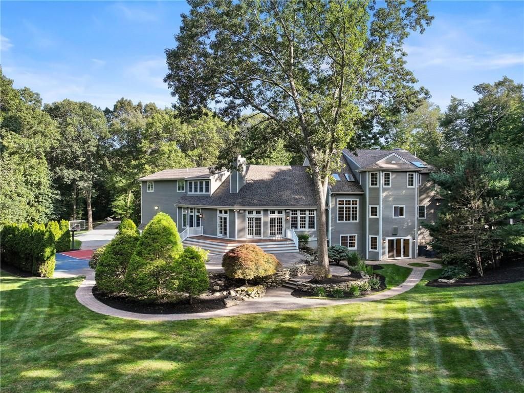 Large gray house with a patio, surrounded by trees and lush green grass.