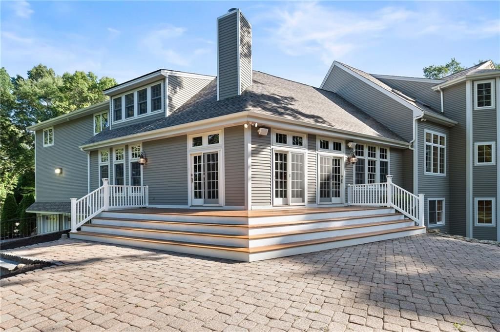 Gray house with a large deck and paver patio. Sunny day with trees in the background.