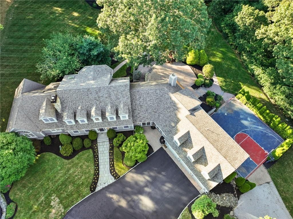 Aerial view of a large house with a stone roof, driveway, and landscaping surrounded by trees.