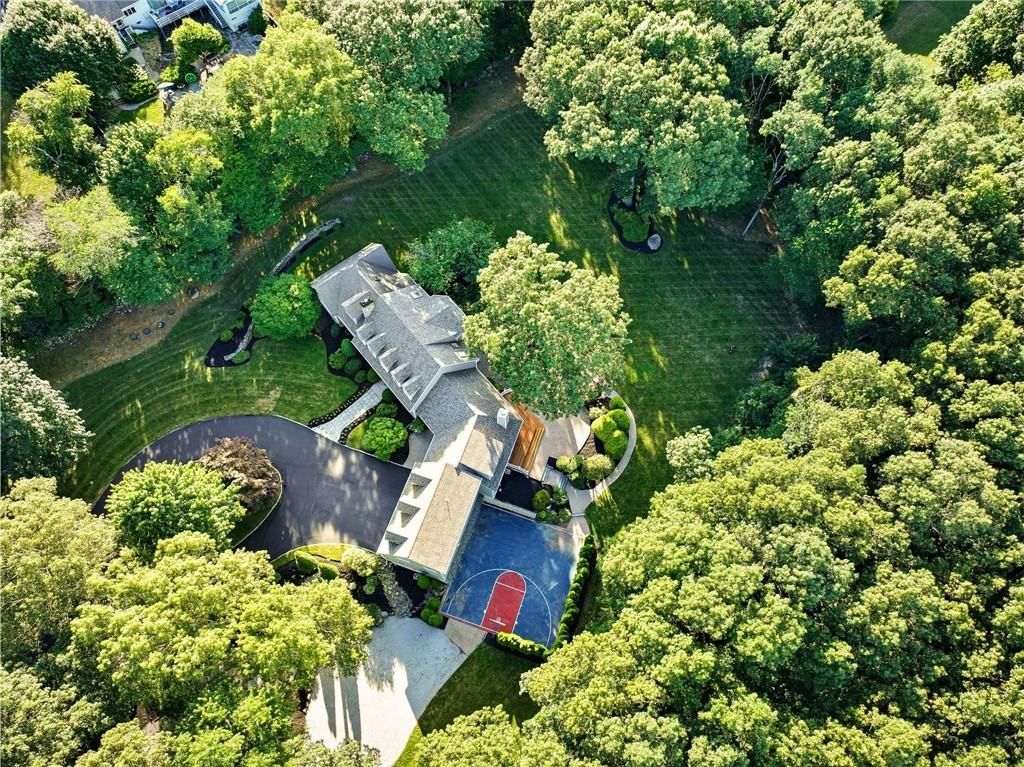 Aerial view of a house nestled among lush green trees, with a long driveway and dark pavement.