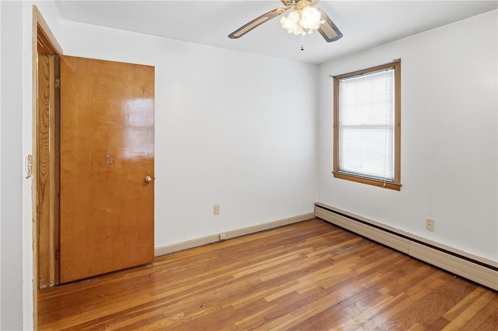 Empty bedroom with hardwood floors, white walls, and a closed wooden door.