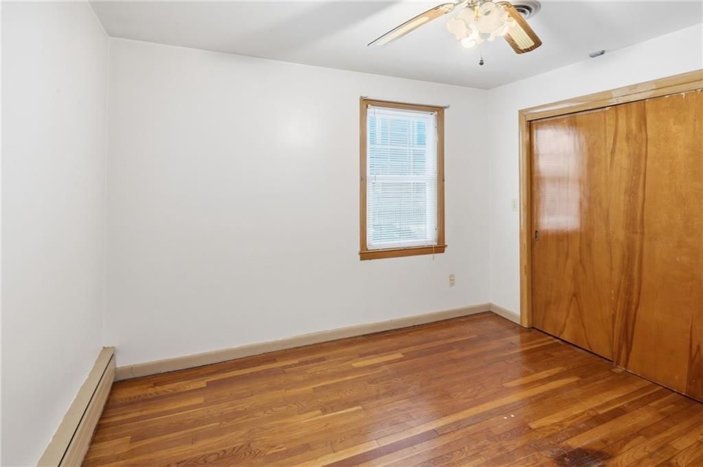 Empty bedroom with hardwood floors, a small window, and a wood closet. White walls.