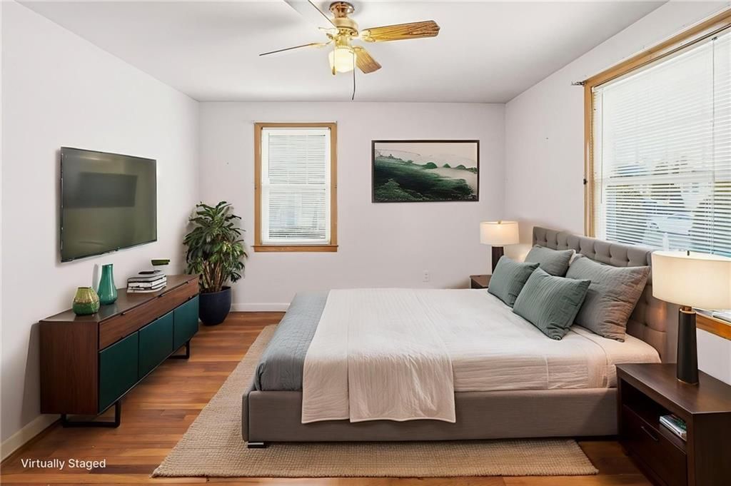 Bedroom with bed, TV, wood floor, and two windows.