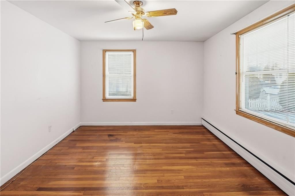 Empty room with wood floors, two windows, and a ceiling fan.
