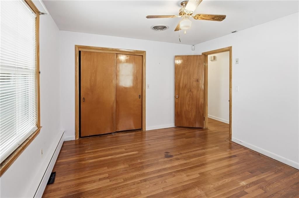 Empty bedroom with hardwood floors, two wooden doors, a window, and a ceiling fan.