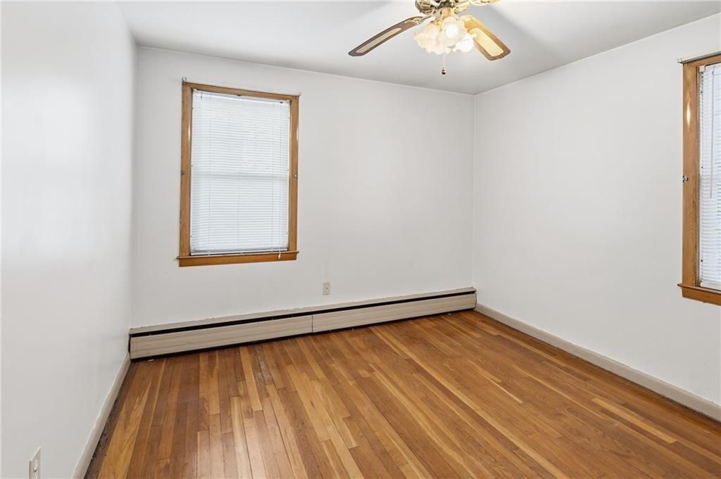 Empty room with wood floors, two windows with blinds, and a ceiling fan.