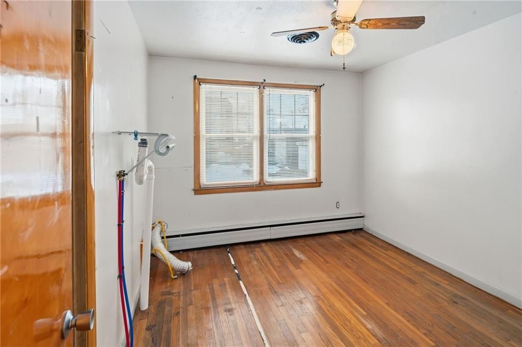 Empty room with hardwood floors, window, ceiling fan, and open door.
