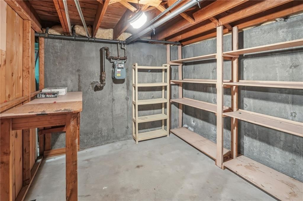 Basement storage room with concrete walls, wooden shelves, a workbench, and exposed ceiling beams.