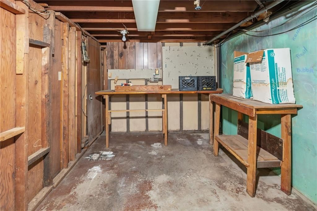 Basement interior with two wooden workbenches, wood-paneled walls, and peeling paint on the concrete floor.