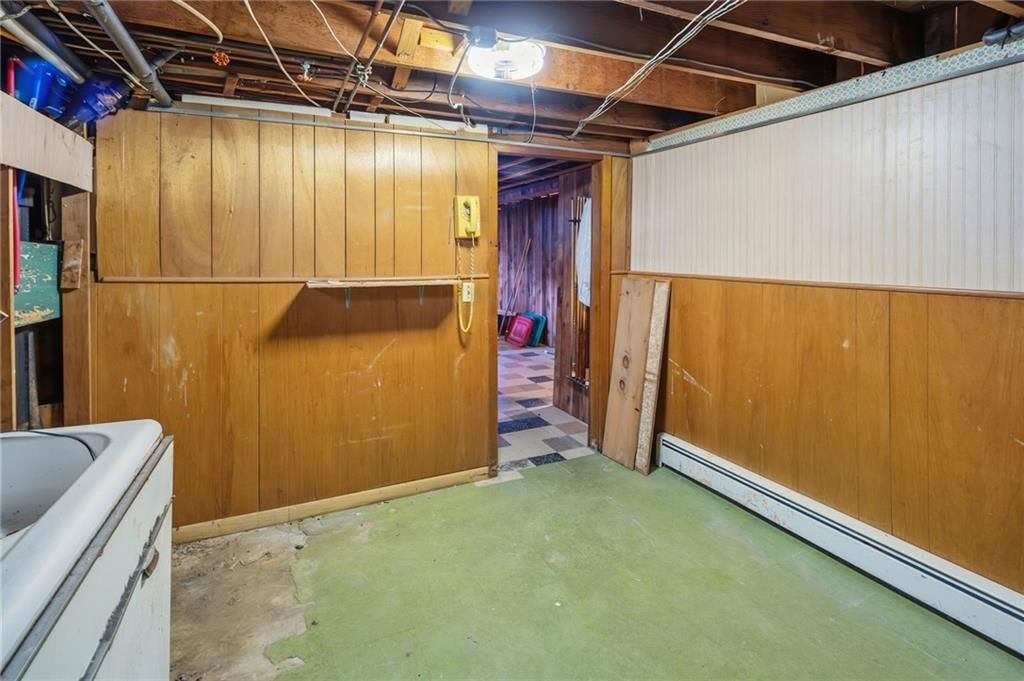 Basement with wood paneling, green carpet, open doorway, exposed beams, and a white appliance.