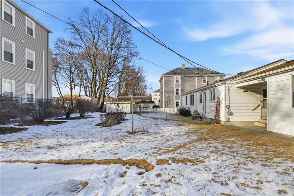 Snow-covered yard between buildings, with power lines overhead. Bare trees, overcast sky.