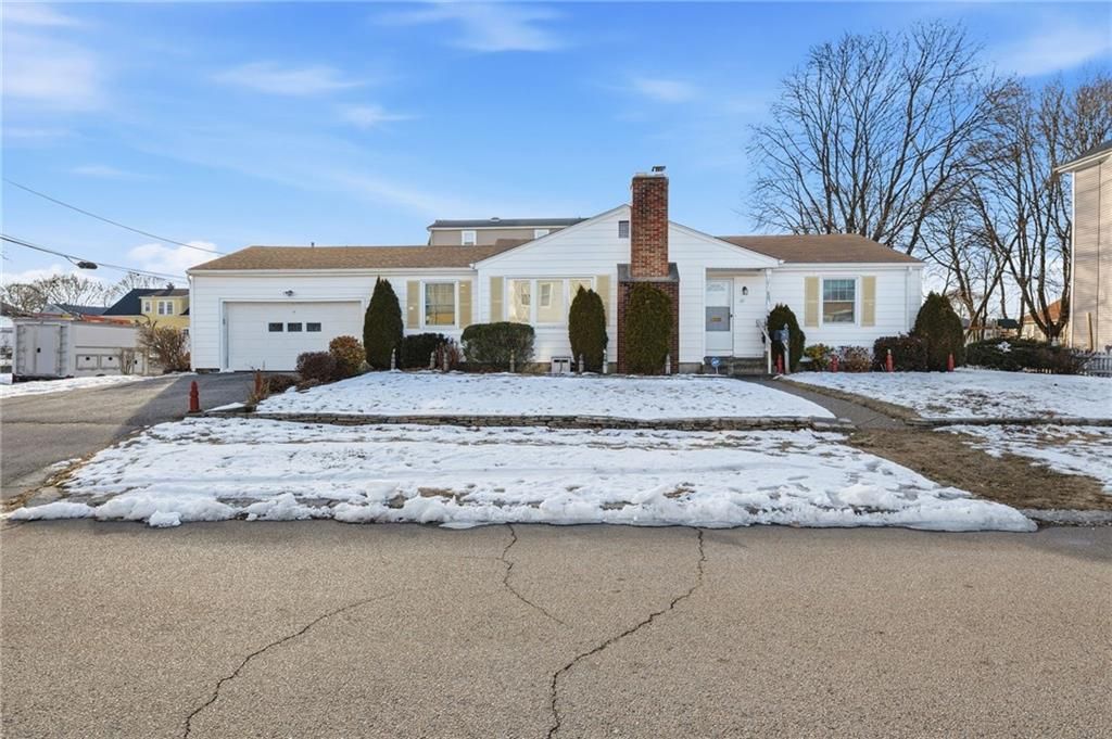 White ranch-style house with a brown brick chimney, snow on the lawn, and a cracked asphalt driveway under a blue sky.