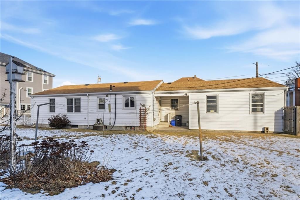 Back of a single-story white house with brown roof on a snow-covered lot under a partly cloudy blue sky.