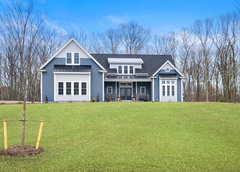 Blue house with white trim, set on a green lawn with a clear blue sky. Trees in the background.