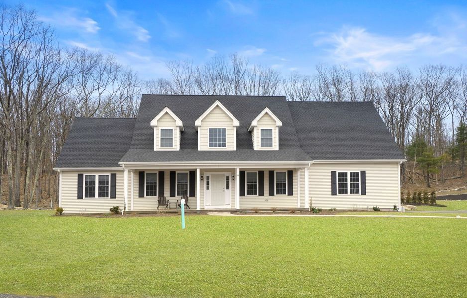 Beige ranch house with black shutters, three dormers, and a large lawn.
