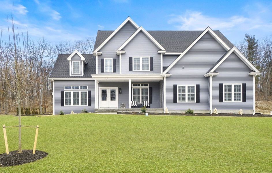 Gray two-story house with black shutters, white trim, and a porch, set on a green lawn with a blue sky.