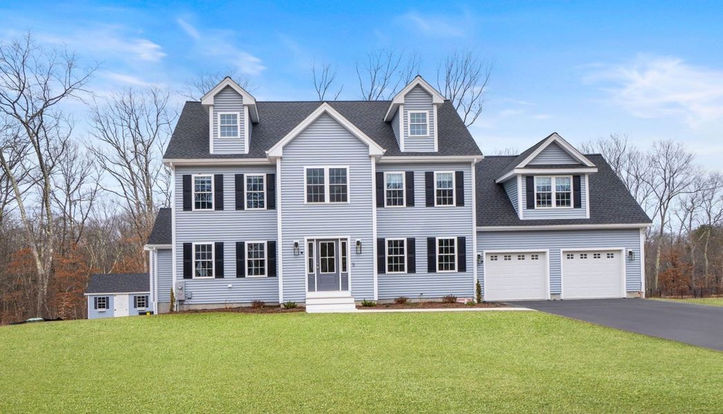 Two-story light blue house with black shutters, three dormers, and a two-car garage under a blue sky.