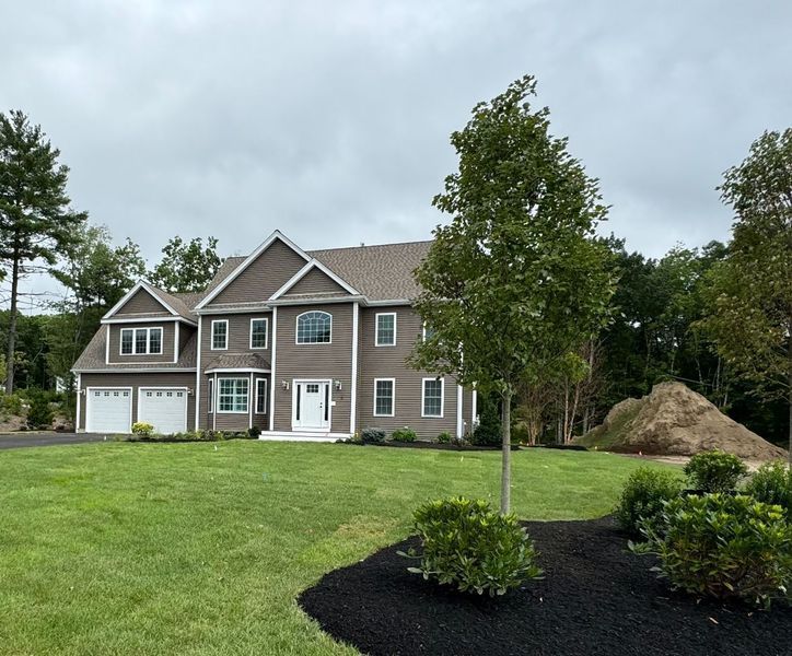 Two-story house with gray siding, white trim, and a manicured lawn under a cloudy sky.