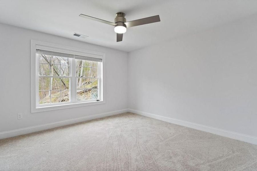Empty bedroom with white walls, window, carpet, and ceiling fan.