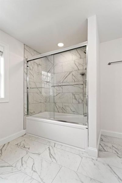 Bathroom with a white bathtub and marble-look tiles. Glass shower doors with chrome hardware.