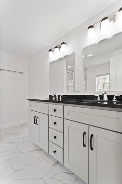 White bathroom with double vanity, black countertop, mirrors, and lighting.
