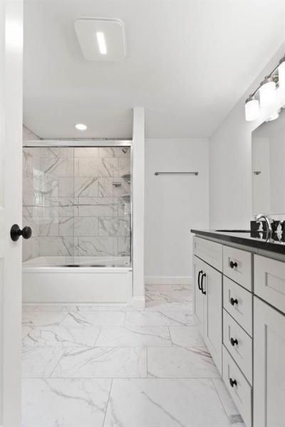 Bright white bathroom with marble tile floor and shower, and white vanity with black hardware.